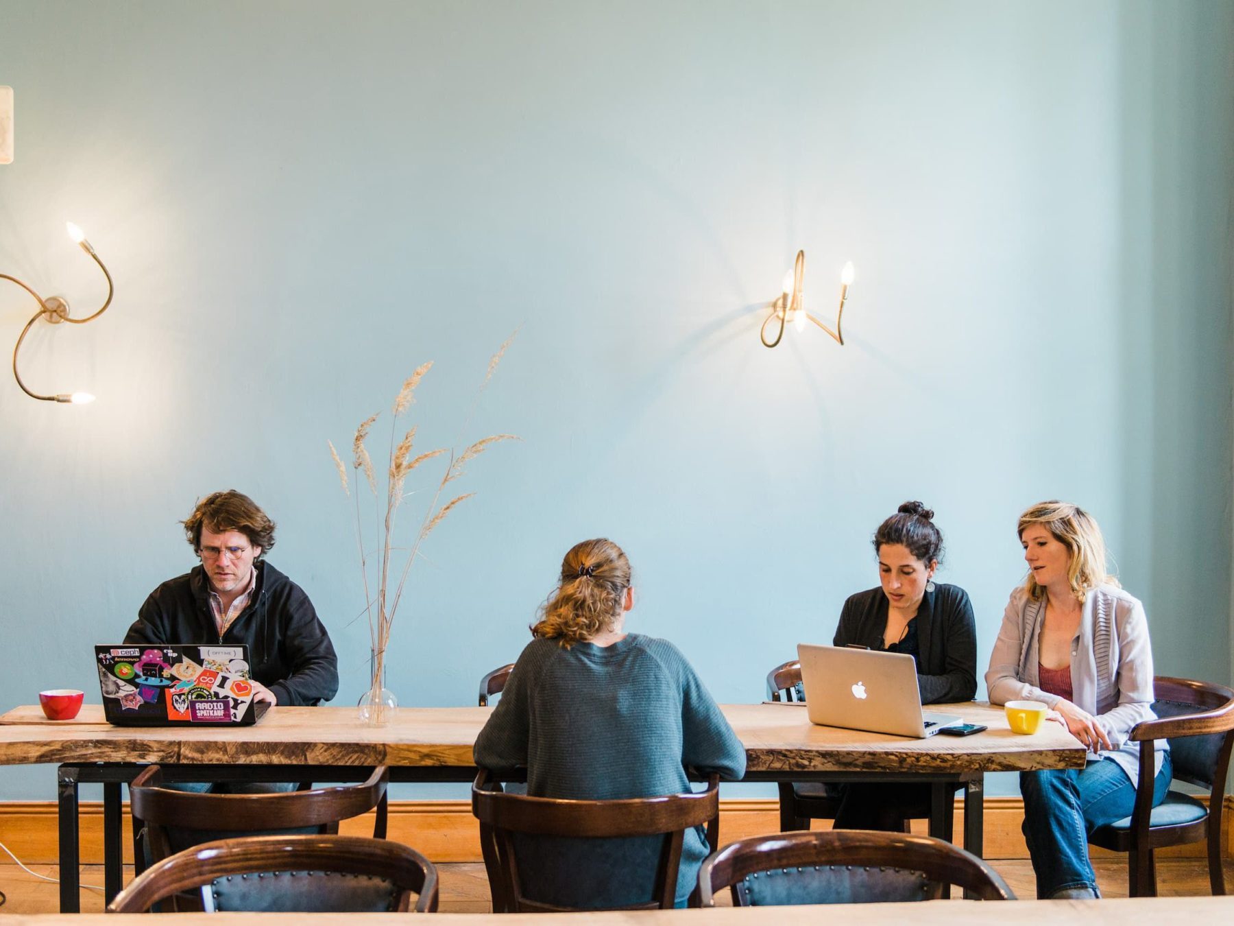 Ein langer Tisch aus Holz, an dem ein Mann und drei Frauen mit Laptop sitzen