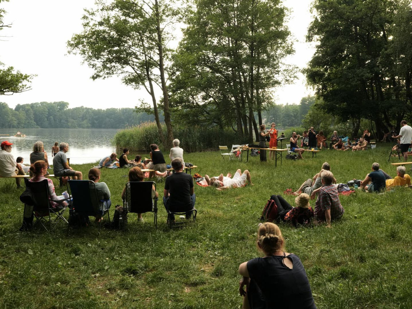 Mehrere Personen auf einer Wiese an einem See einem Konzert lauschend