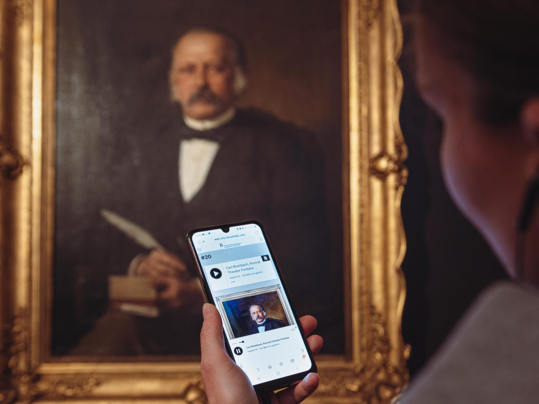 Eine Person, die ein Smartphone in der Hand hält und ein Museumsobjekt ansieht