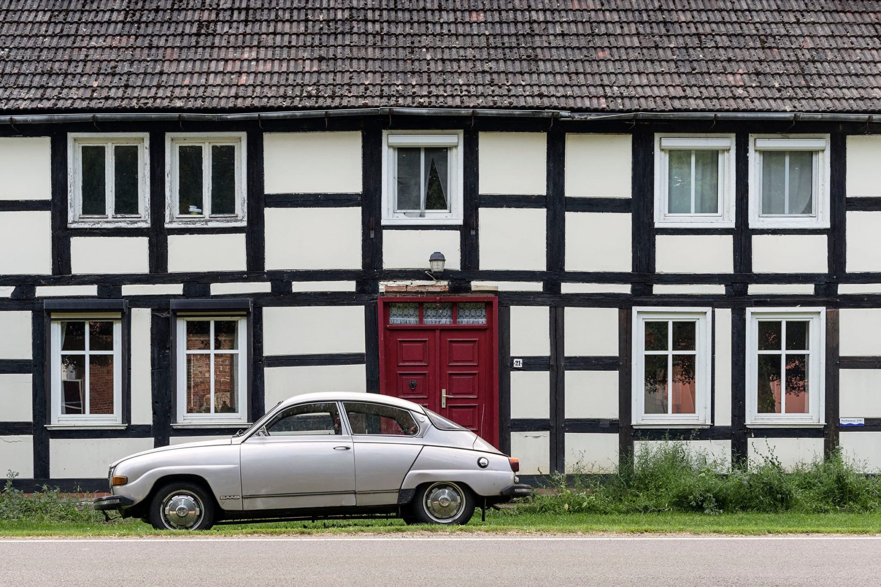 Fachwerkhaus mit einer roten Tür, davor steht ein altertümlich anmutendes Auto