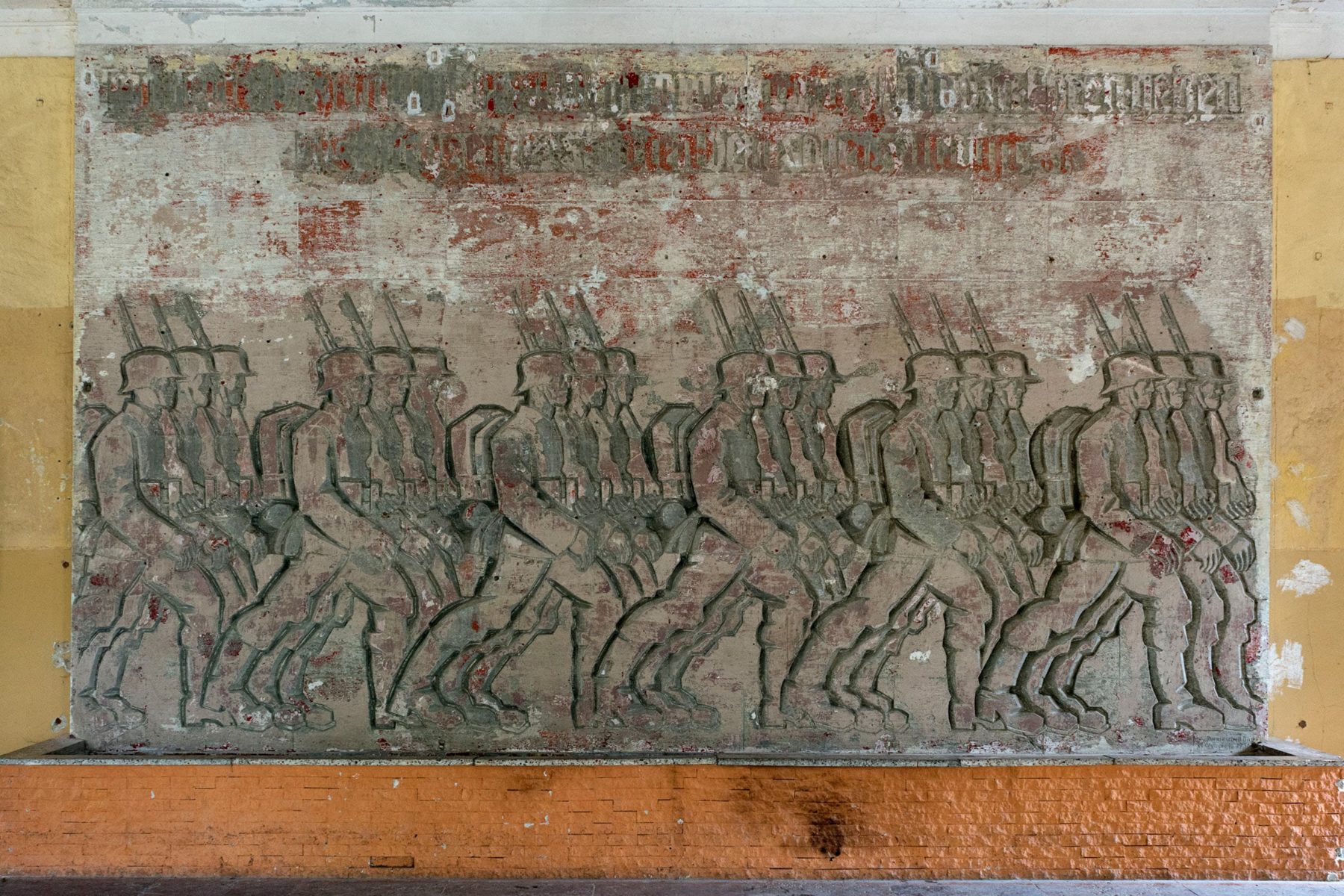 Wandrelief mit marschierenden Wehrmachtssoldaten, die Überschrift des Reliefs wurde abgeschabt
