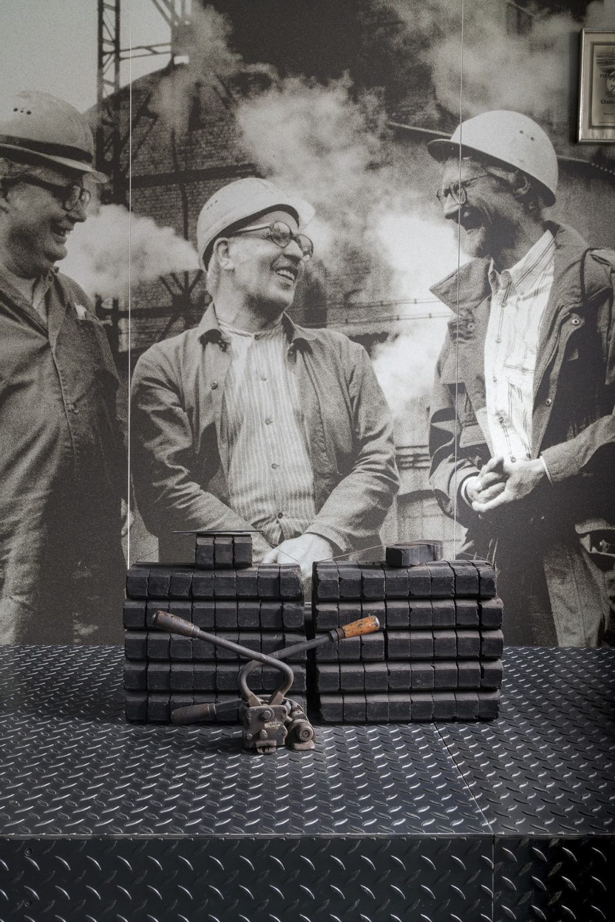 Ausstellungsbild mit Menschen in der Kohle, davor gestapelte Kohlebriketts