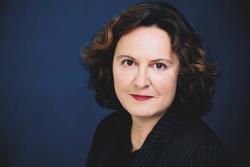Ein Portraitfoto einer weiblichen Person mit dunklen, lockigen Haaren Haaren vor einem dunkelblauen Hintergrund.