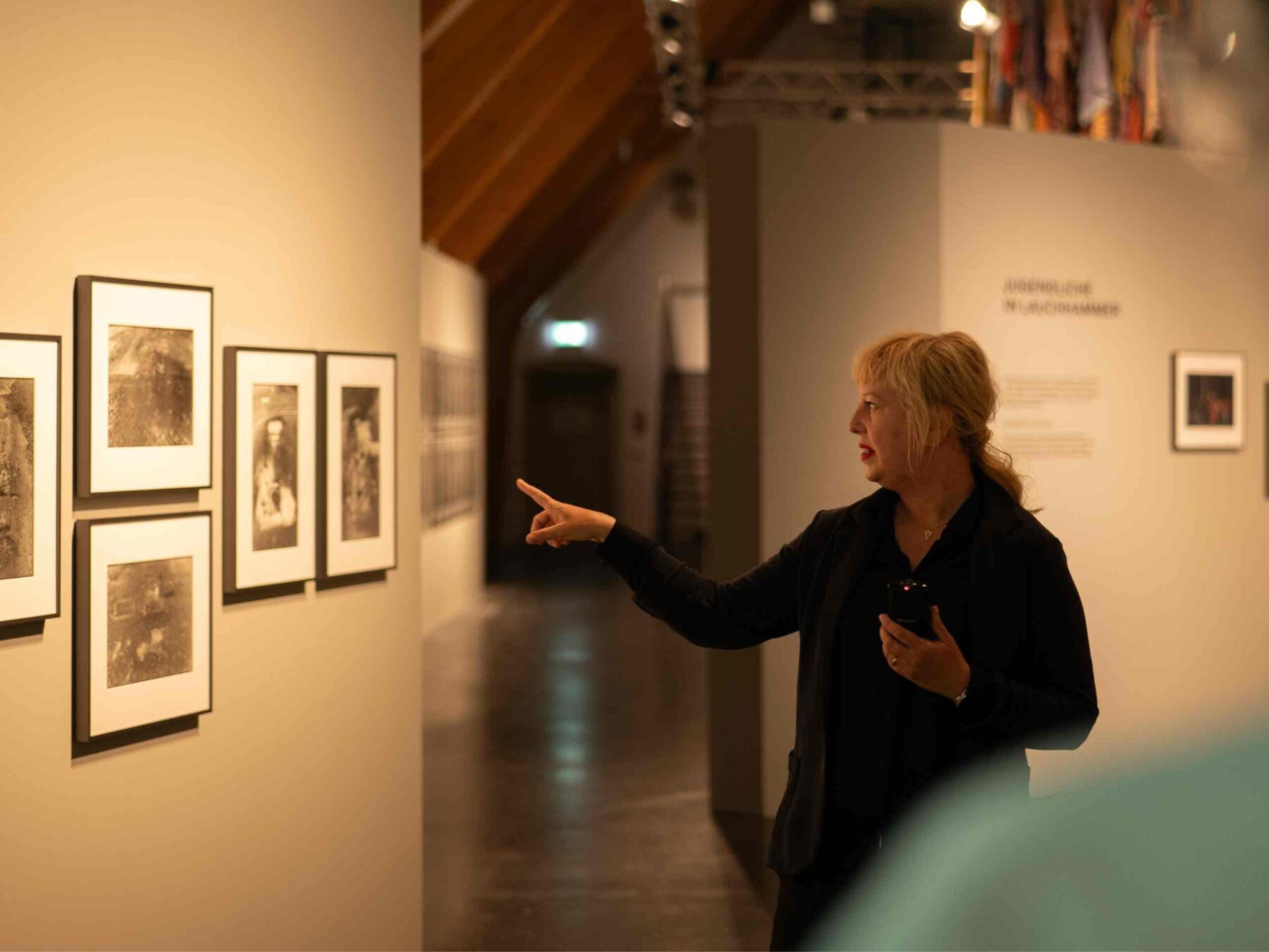 Führung in der Ausstellung, dunkel gekleidete Frau zeigt auf Bilder