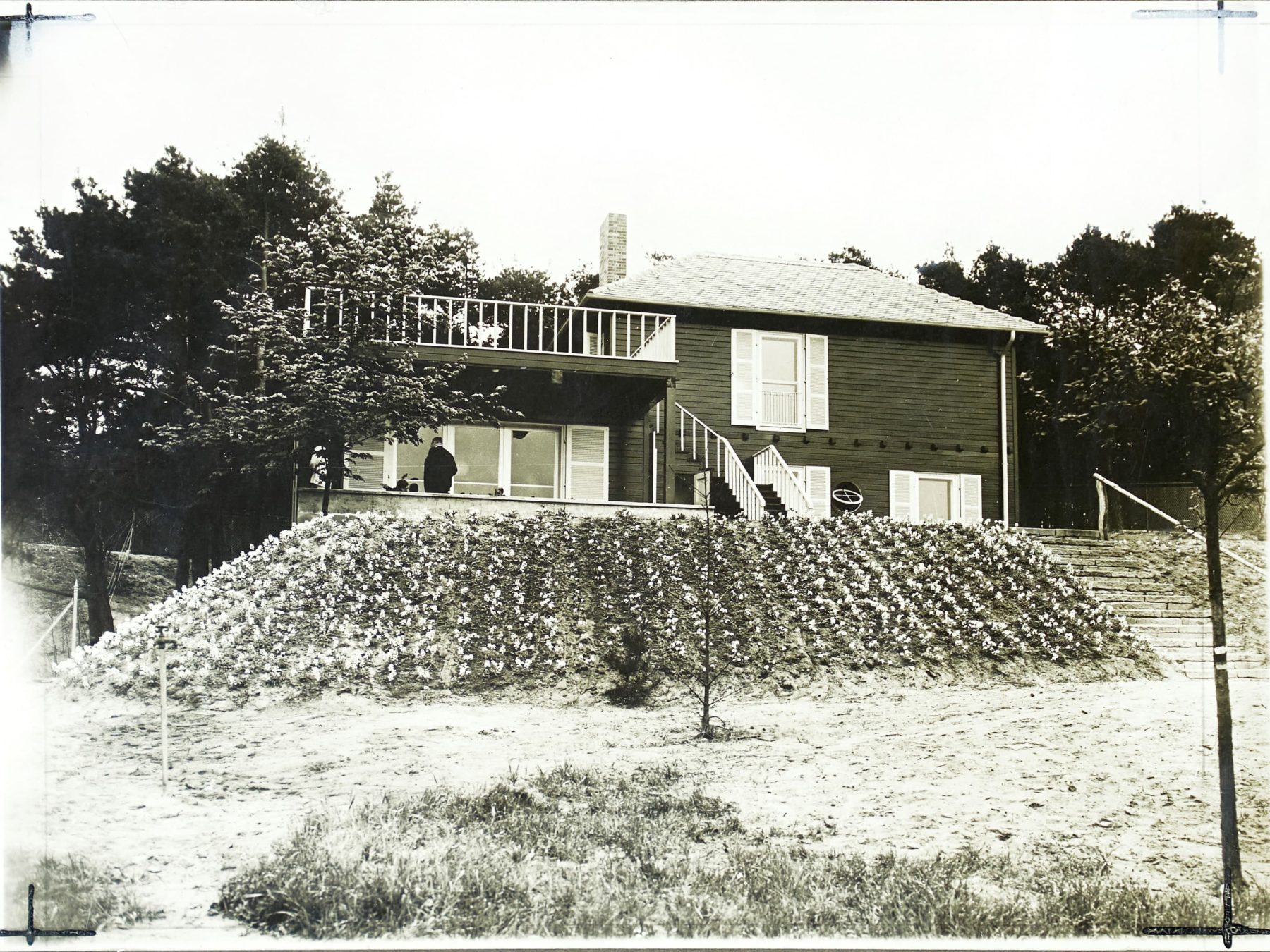 Schwarz-weiß Fotografie mit einem Haus und Blumengarten davor.