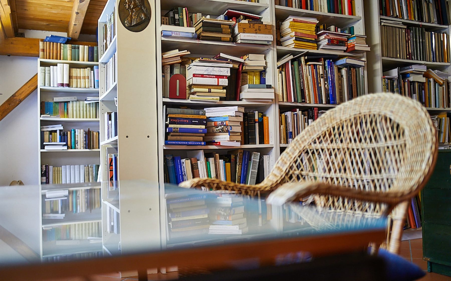 Im Vordergrund ein Glastisch und ein Korbsessel, im Hintergrund hohe Bücherregale