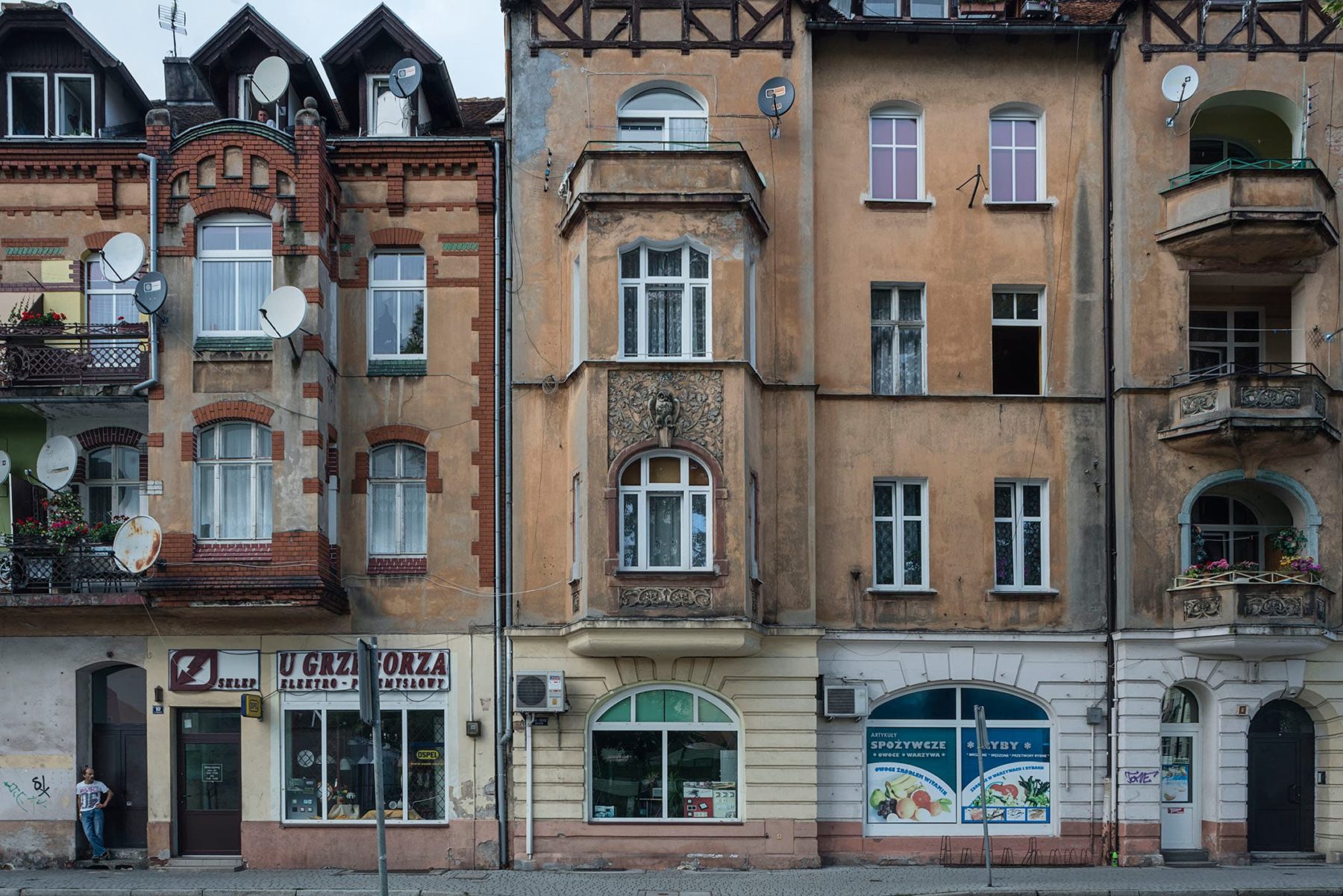 Fassade zweier hsitorischer Wohnhäuser aus der Gründerzeit, im Erdgeschoss Werbung von verschiedenen Geschäften