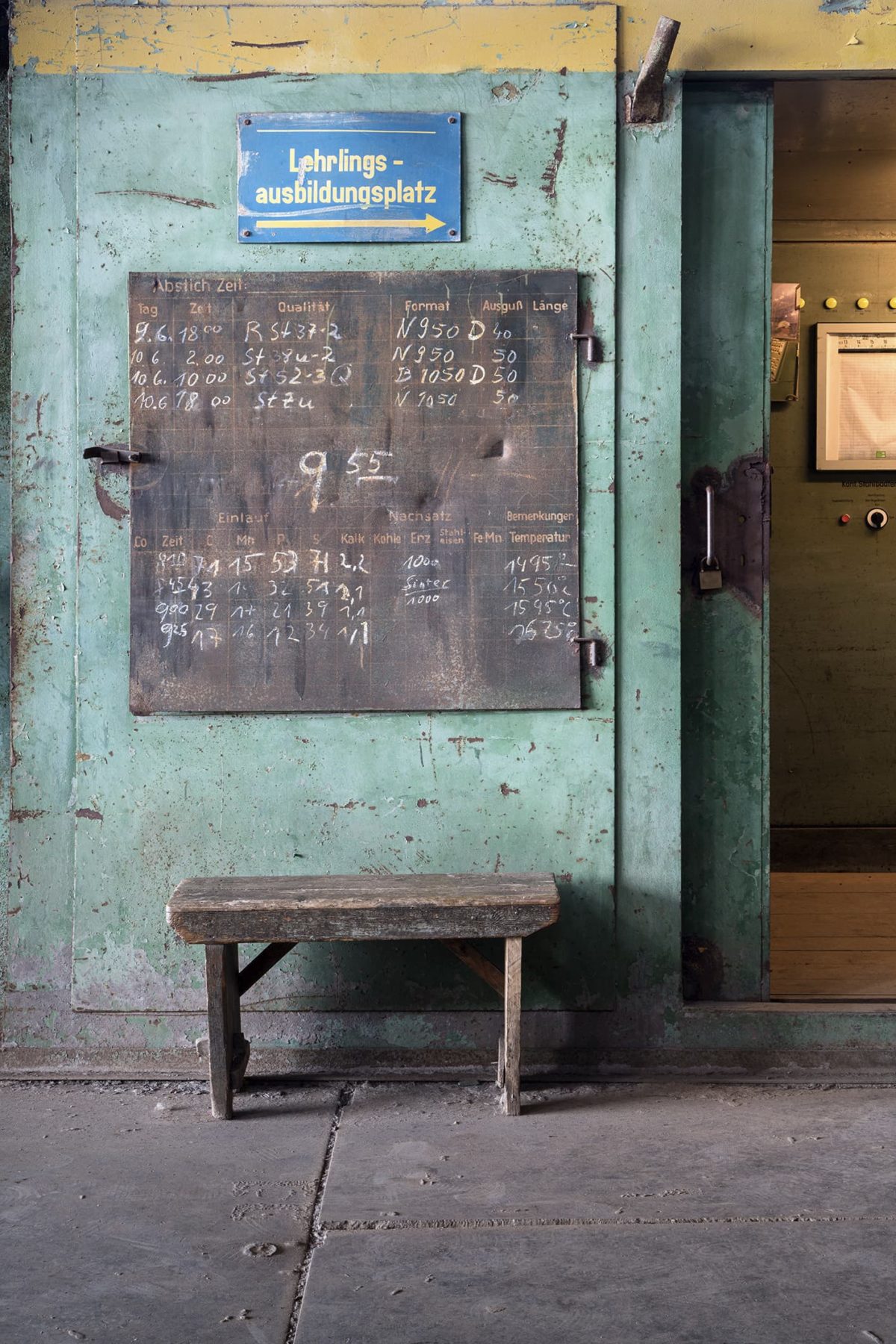 Tafel mit Terminen zur Lehrlingsausbildung an einer grünen Wand, davor eine kleine Holzbank