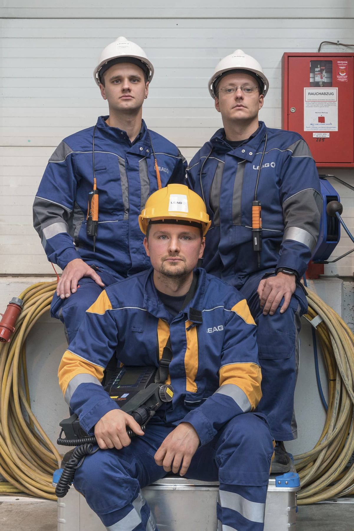 Drei Männer in blauer Arbeitsschutzkleidung und Schutzhelmen
