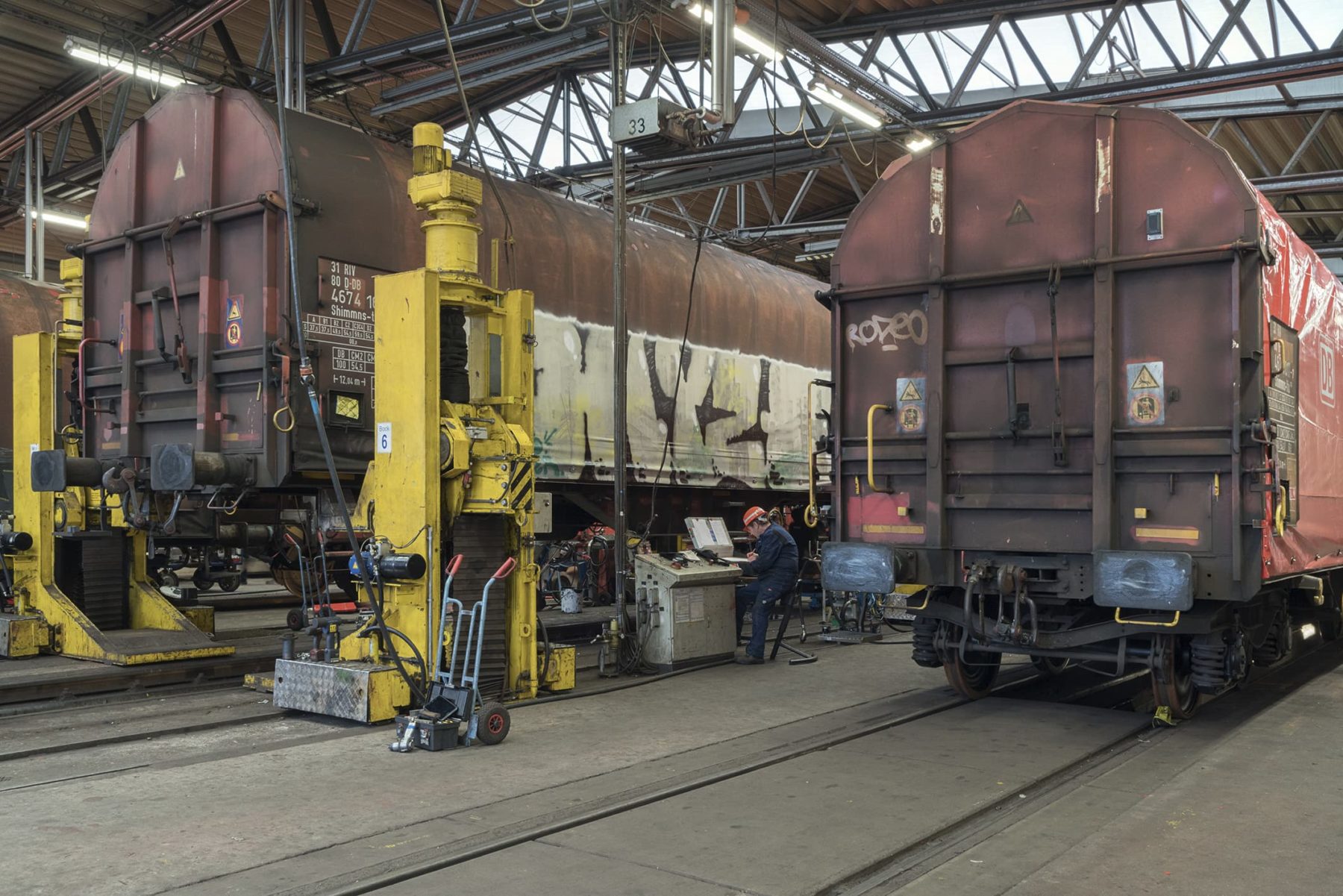 Güterwaggons in einer Halle, einer der Waggons steht auf einer Hebebühne aus gelben Stahlträgern