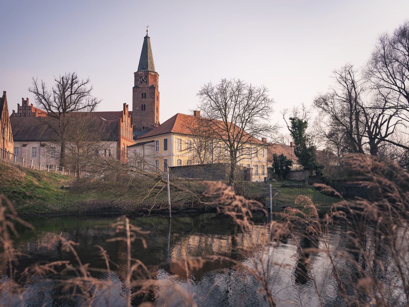 Foto vom Flußufer auf eine Insel mit verschiedenen historischen Gebäuden und einem Kirchturm