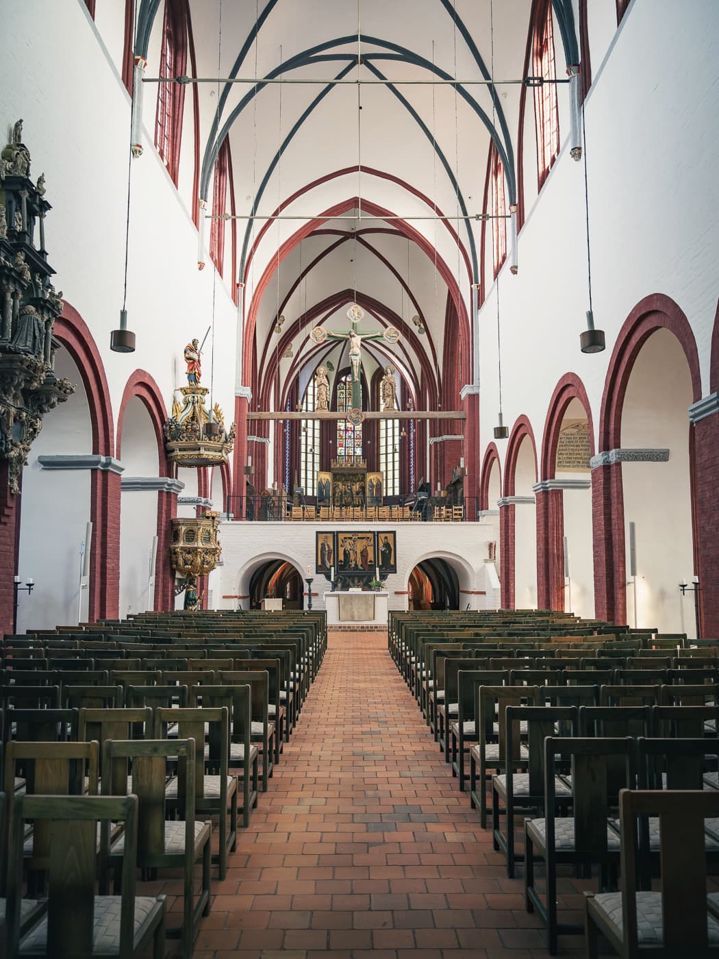 Innenraum einer Kirche mit Rund- und Spitzbögen, vielen Stühlen und einem Altar.
