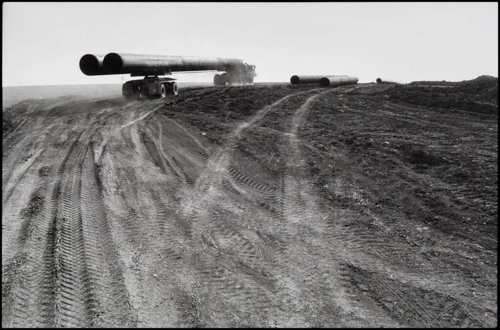 Schwarz-weiß Bild, LKW transportiert lange Rohrleitungen auf einem sandigen Untergrund
