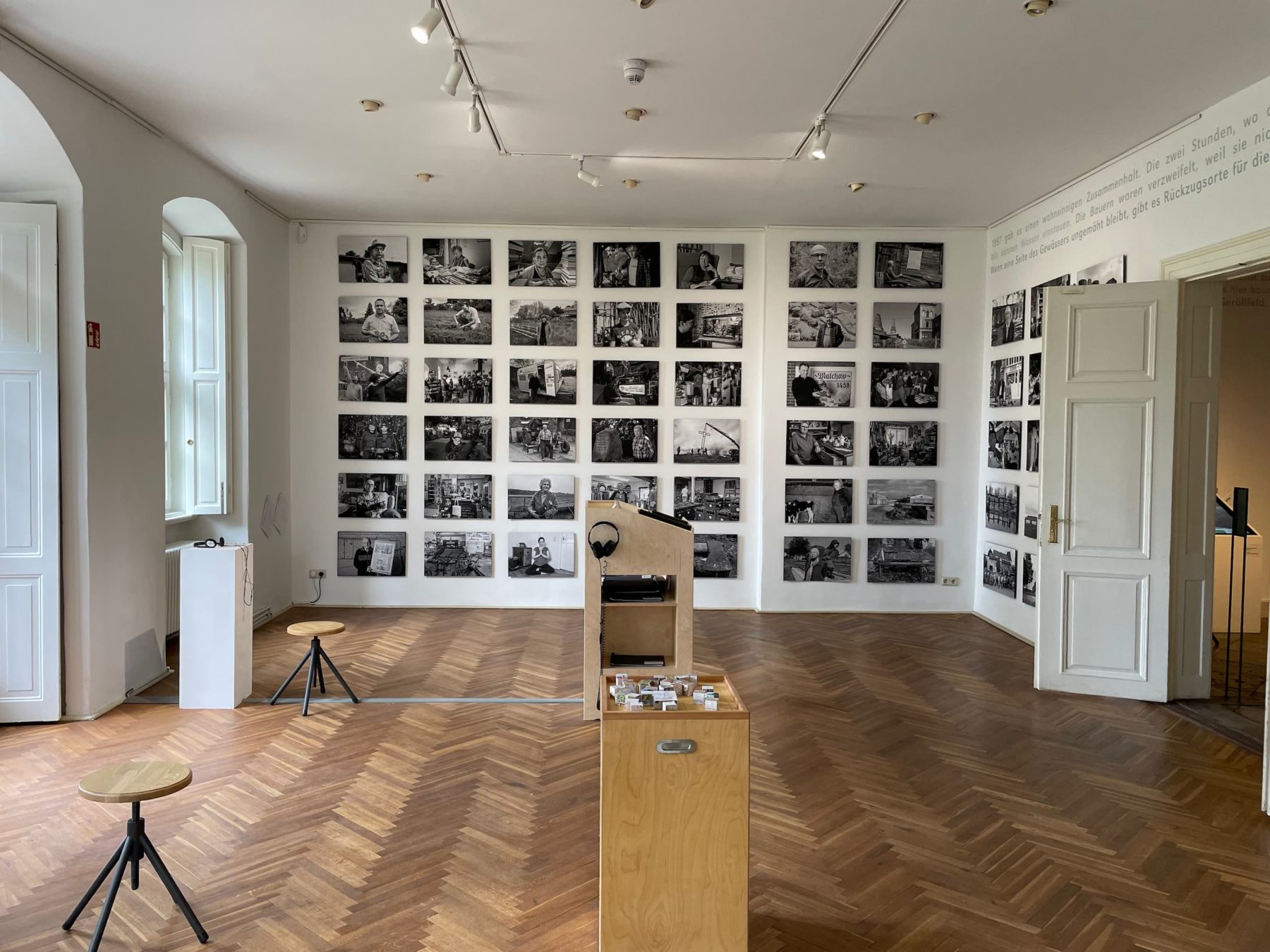 Raum mit vielen schwarz-weiß Bildern an den Wänden, links und rechts sind weiße Türen zu sehen, die offen stehen.