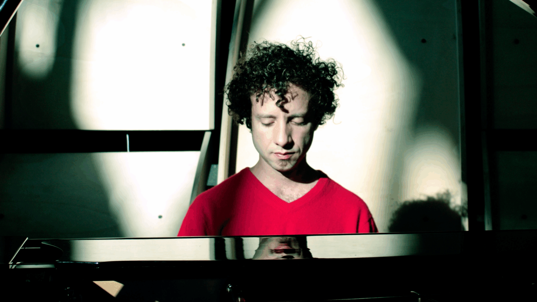 Eine Person sitzt hinter einem Klavier und trägt ein rotes Shirt